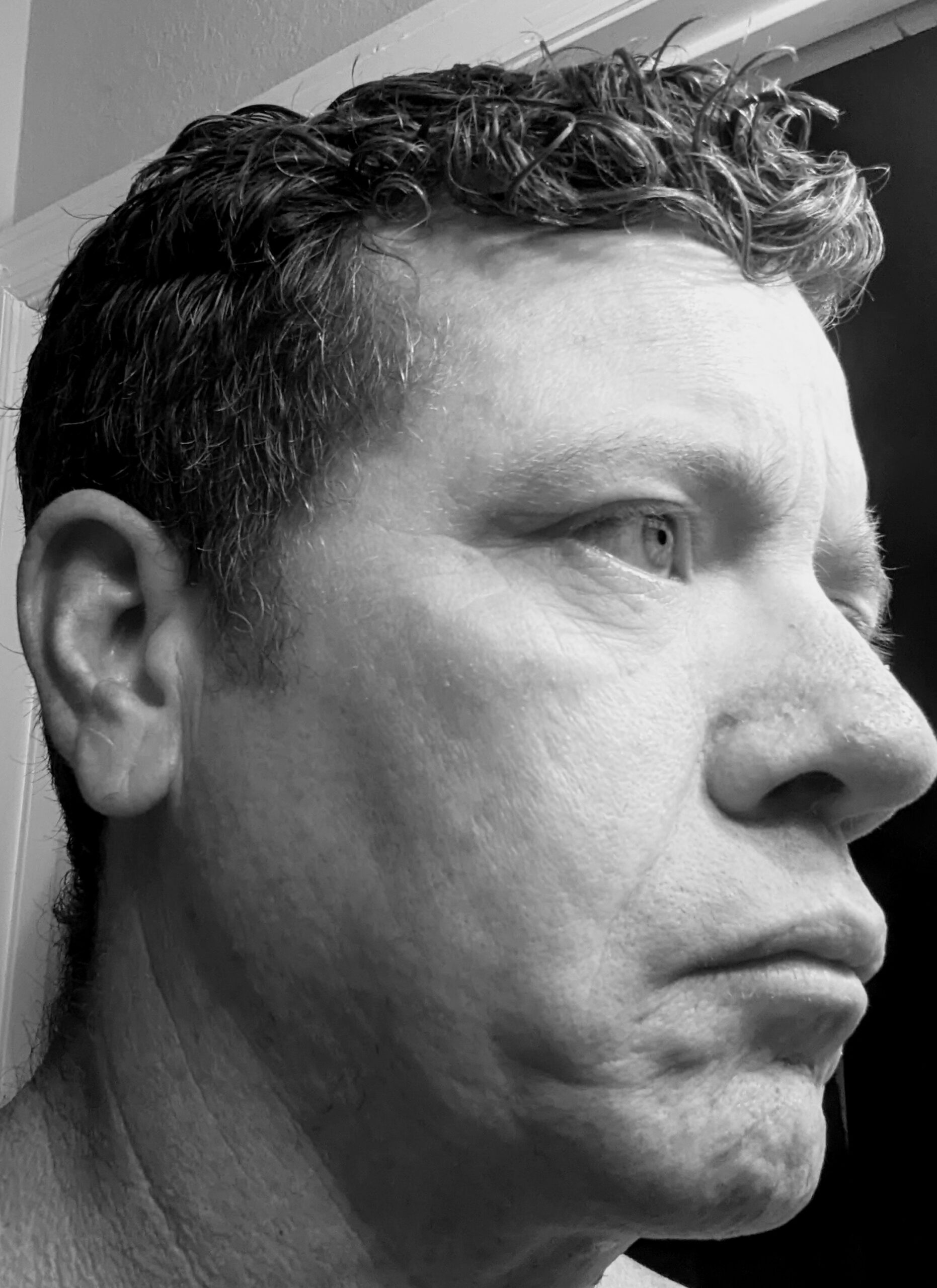 A profile view of a man with short, curly hair, displaying facial features and a serious expression. The monochrome tone highlights textures.