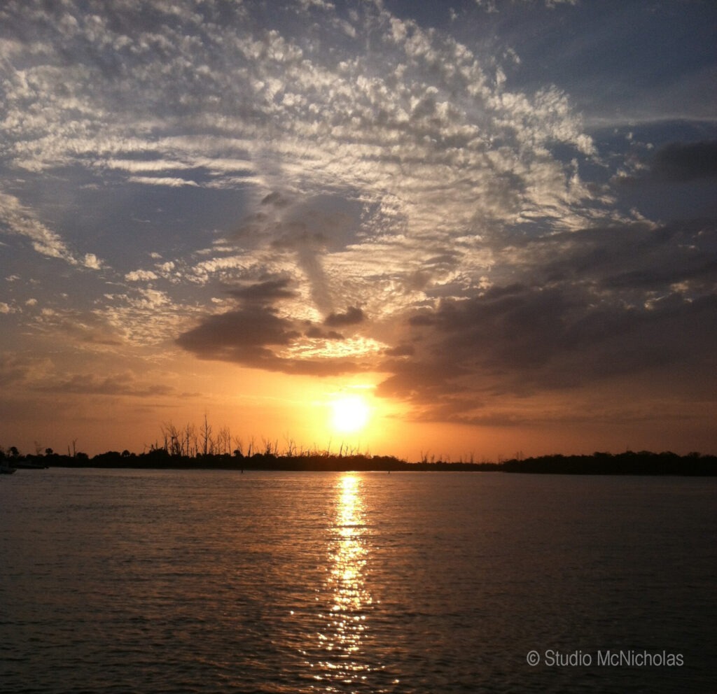 Vibrant sunset reflects on tranquil water, with silhouetted trees in the background, capturing the serene beauty of nature.