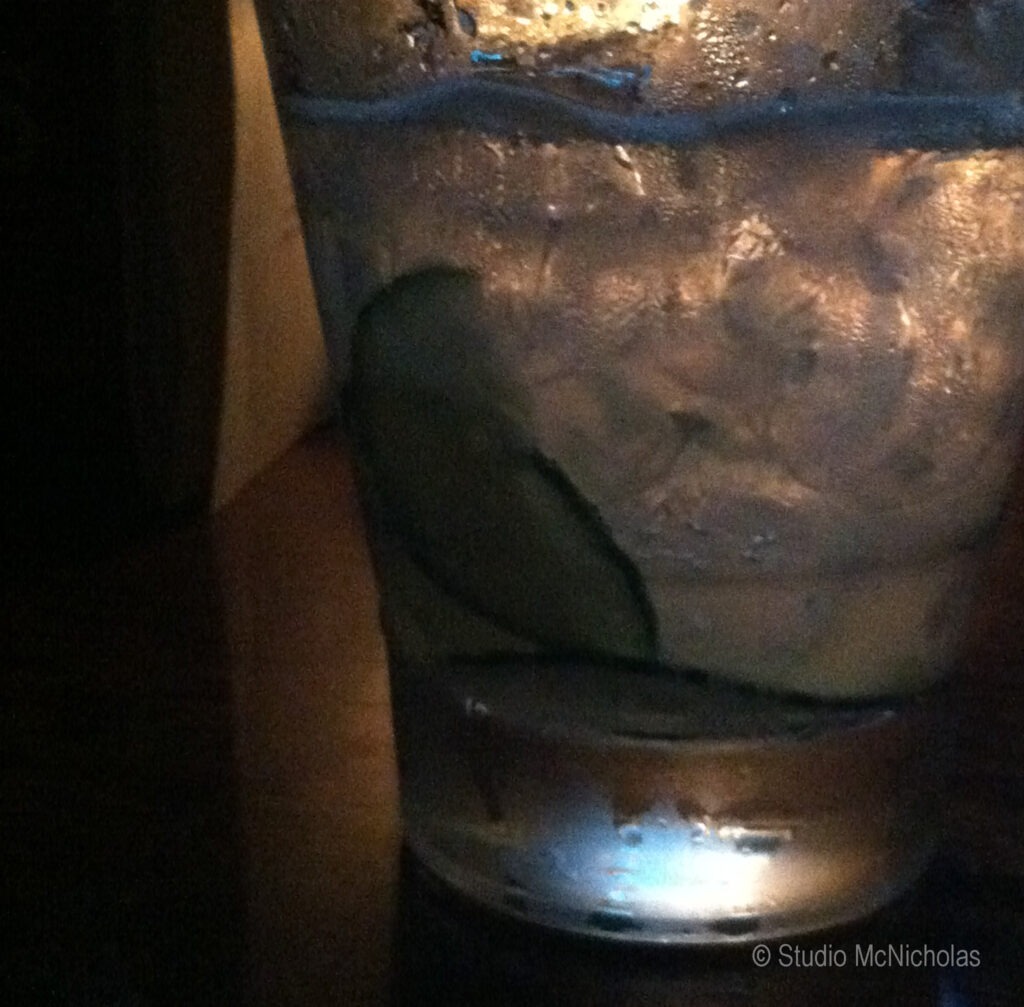 Crisp glass filled with water and cucumber slices, illuminated softly on a dark table, highlighting a refreshing drink setting.