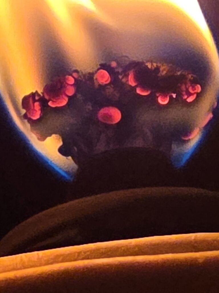 Flame from a torch, highlighting glowing red embers atop a dark material, creating a striking contrast against the orange and blue hues of the fire.