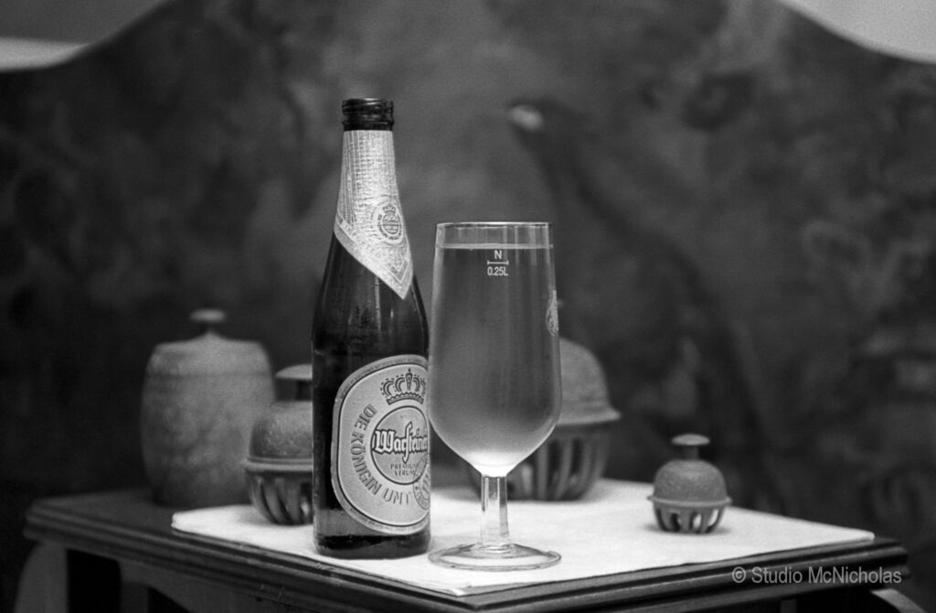 A bottle of Waagfelder beer is displayed next to a clear glass filled with beer, set on a table with decorative objects in the background.