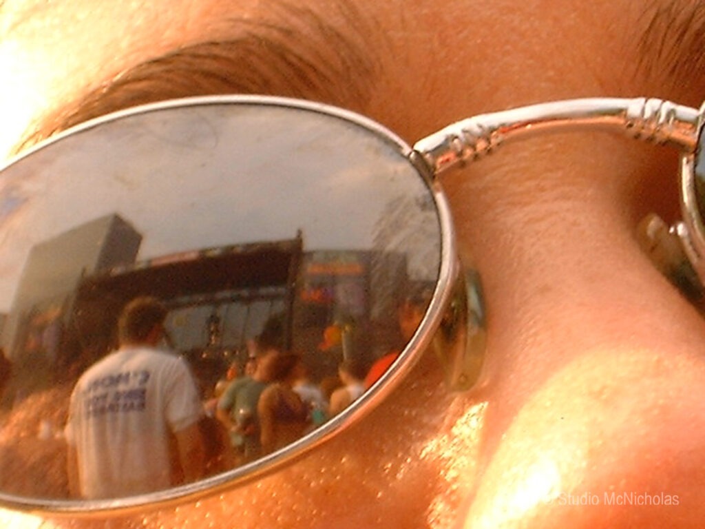 Reflection of a concert crowd visible in the sunglasses of a person, capturing the vibrant atmosphere of a live music event.