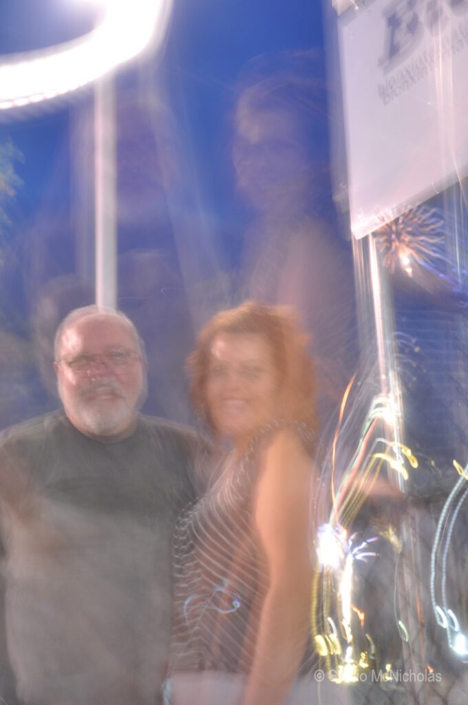 A blurry photo captures a man and a woman posing together, surrounded by colorful lights and a festive atmosphere, suggesting a lively event.