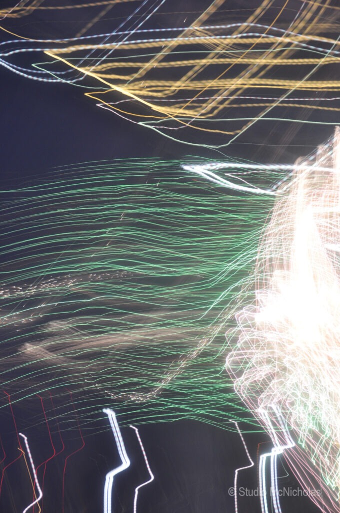 Colorful, blurred light trails create a dynamic, abstract pattern against a dark background, showcasing movement and energy typical of festive events.