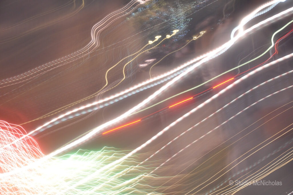 Abstract light trails create dynamic, swirling patterns against a dark background, depicting movement and energy in a nighttime urban setting.
