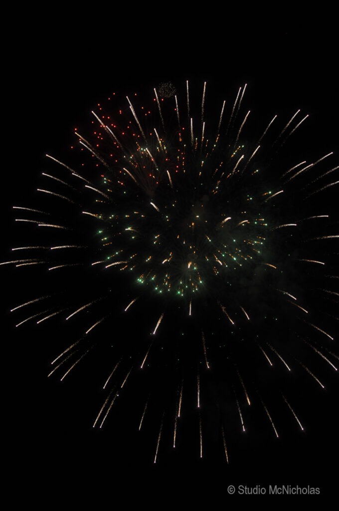 Colorful fireworks burst against a dark sky, showcasing vibrant reds, greens, and whites, celebrating a festive occasion.