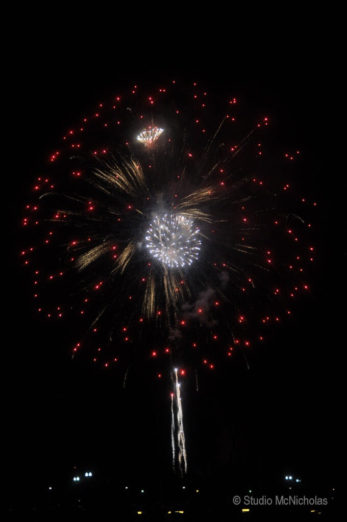Colorful fireworks burst in the night sky, featuring spirals of red and white sparks, against a dark backdrop, celebrating a festive occasion.