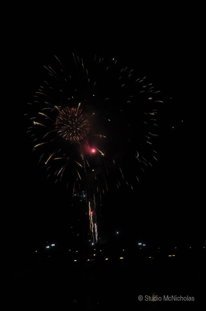 Colorful fireworks burst against a night sky, illuminating the scene with vibrant sparks. The image captures the excitement of a celebration.