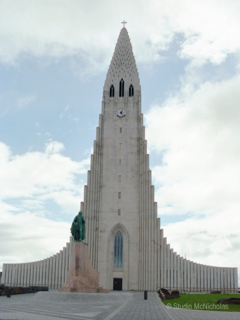 Hallgr&iacute;mskirkja, a prominent church in Reykjavik, features a striking steeple and nearby statue of Leif Erikson, set against a cloudy sky.