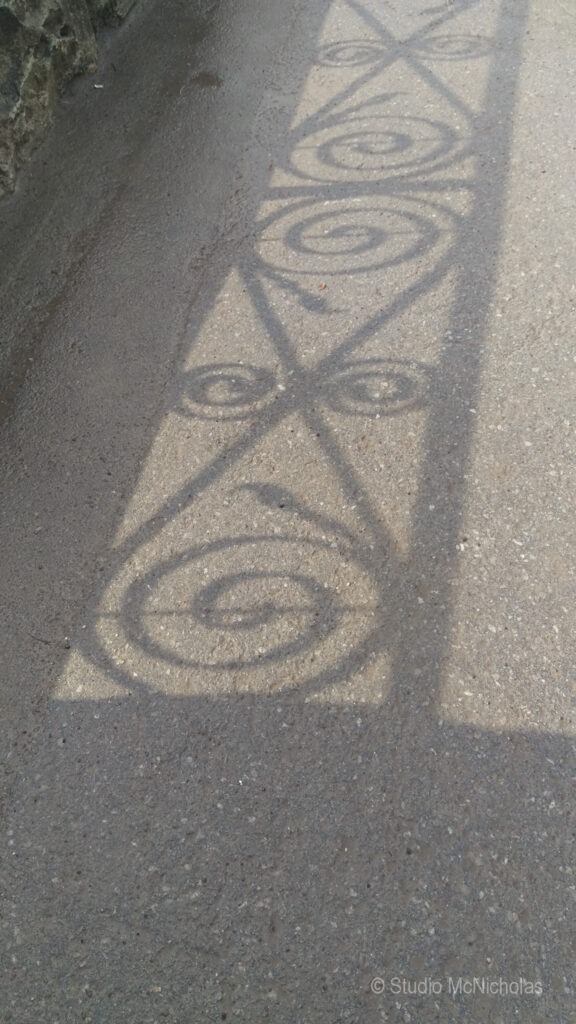 Swirling shadow patterns cast onto a textured pavement, creating an artistic effect. This image highlights the beauty of light and shadow interplay.