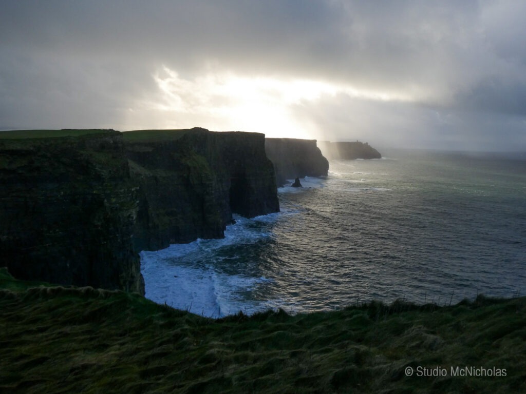 Dramatic cliffs meet turbulent ocean waves under a moody sky, capturing the rugged beauty of Ireland's coastline. A serene yet powerful landscape.