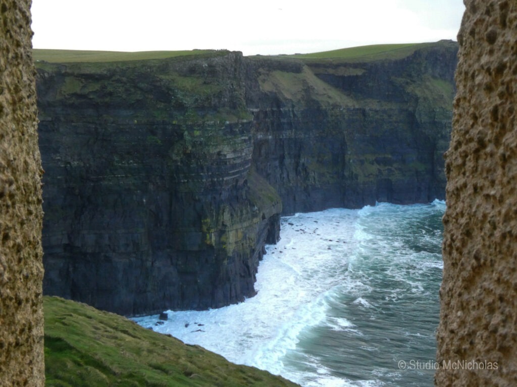 Cliffs rise dramatically above turbulent ocean waves, framed by textured stone edges, highlighting the natural beauty of the coastline.