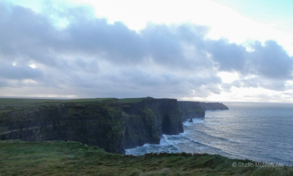 Cliffs of Moher majestically rise above the Atlantic Ocean, showcasing rugged rock formations and vibrant coastal scenery under a cloudy sky.
