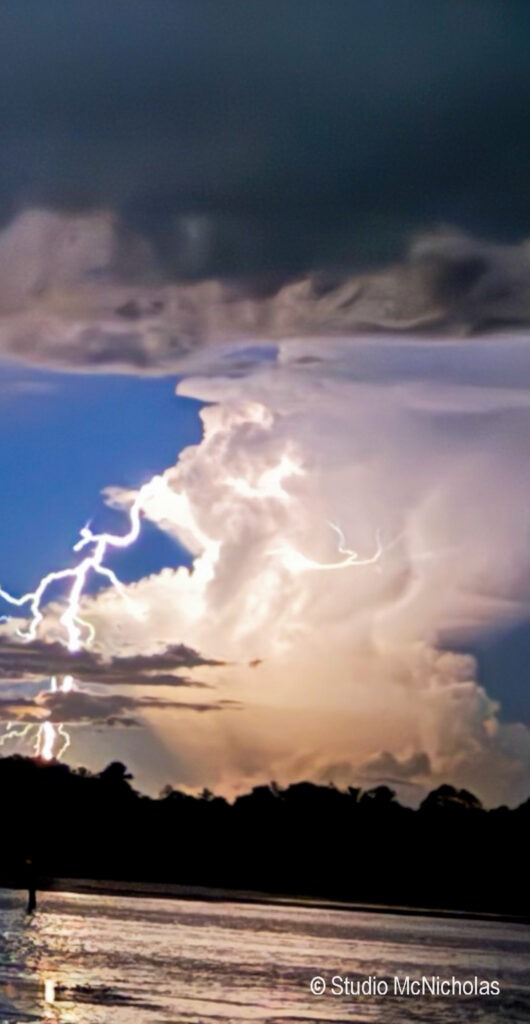Lightning strikes illuminate a dramatic cloud formation at dusk, reflecting in the water below, showcasing nature's power and beauty.
