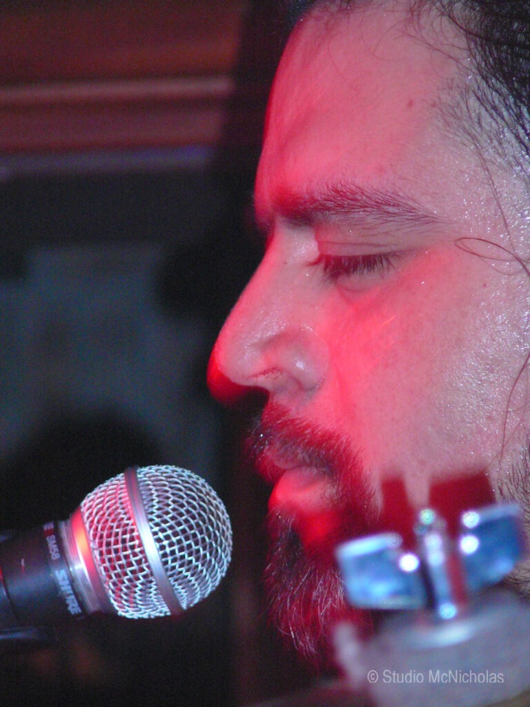 Close-up of a musician passionately singing into a microphone, illuminated by red lighting, capturing the intensity of a live performance.