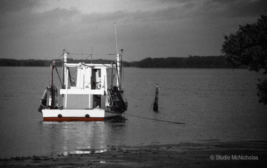 Fishing boat anchored in still water during twilight, showing serene coastal landscape with a distant tree line. Perfect for marine-themed content.